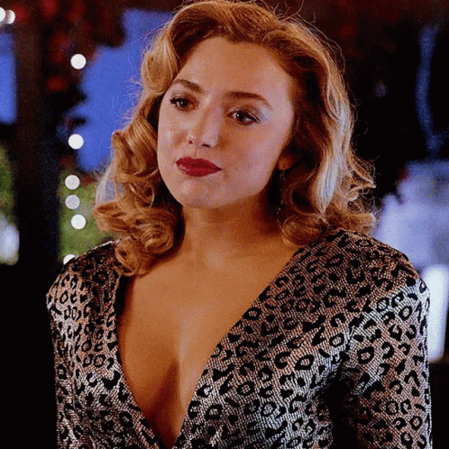 A Woman In A Leopard Print Dress With A Plunging Neckline Looks At The Camera GIF