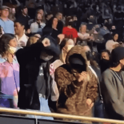 A Woman In A Leopard Print Hoodie Stands In A Crowd Of People Wearing Face Masks GIF