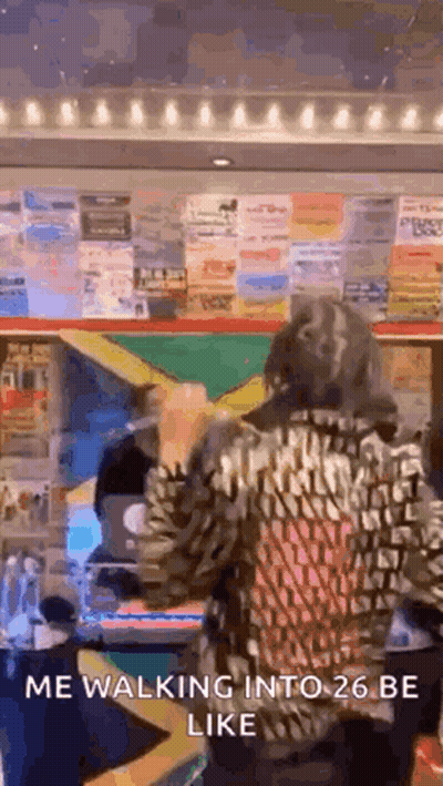 A Woman In A Leopard Print Jacket Is Walking Into A 26 Be Like Sign . GIF