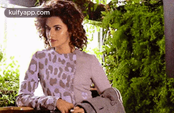 A Woman In A Leopard Print Sweater Is Sitting At A Table In Front Of A Window . GIF