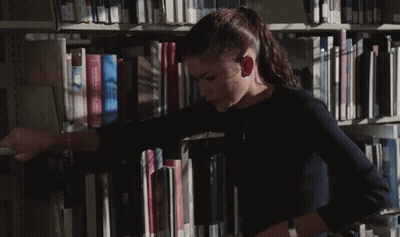 A Woman In A Library Reaches For A Book That Says Visa On The Spine GIF