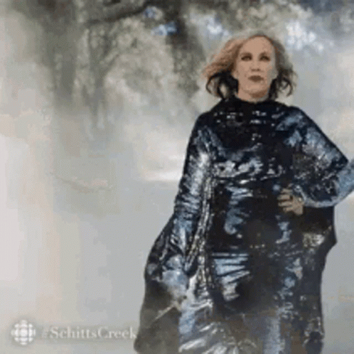 A Woman In A Long Black Dress Is Walking Down A Foggy Street . GIF