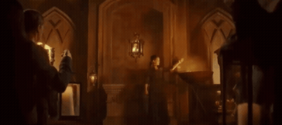 A Woman In A Long Dress Is Standing In A Room With Candles And A Torch . GIF