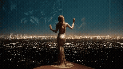 A Woman In A Long Dress Is Standing In Front Of A City Skyline At Night . GIF