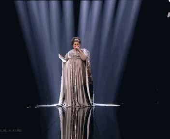 A Woman In A Long Dress Singing Into A Microphone On A Stage With The Hashtag Serbia #Srb GIF