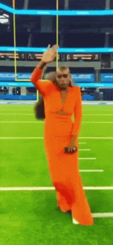 A Woman In A Long Orange Dress Is Dancing On A Football Field GIF