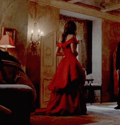 A Woman In A Long Red Dress Is Standing In A Room GIF