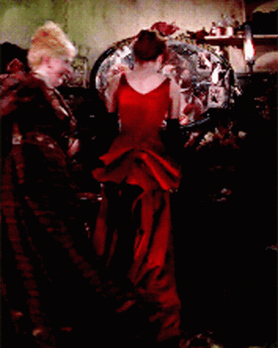 A Woman In A Long Red Dress Is Standing In Front Of A Mirror GIF