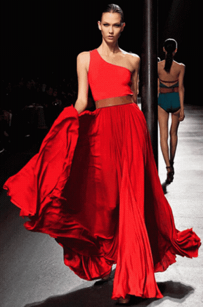 A Woman In A Long Red Dress Is Walking Down A Runway GIF