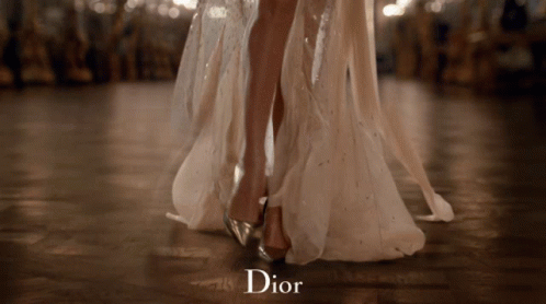 A Woman In A Long White Dress Is Dancing And The Word Dior Is On The Bottom GIF