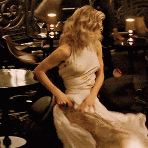 A Woman In A Long White Dress Is Dancing In A Dark Room GIF