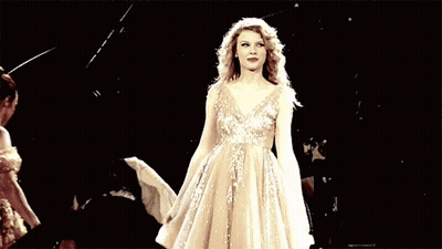 A Woman In A Long White Dress Is Dancing On A Stage In Front Of A Crowd . GIF