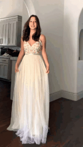 A Woman In A Long White Dress Is Standing In A Room GIF