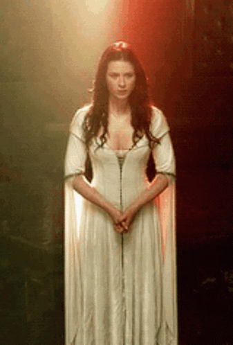 A Woman In A Long White Dress Is Standing In Front Of A Red Light . GIF