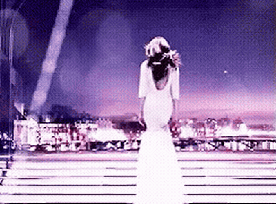 A Woman In A Long White Dress Is Standing On A Stage . GIF