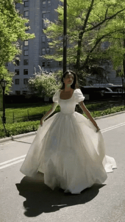 A Woman In A Long White Dress Is Walking Down A Street GIF