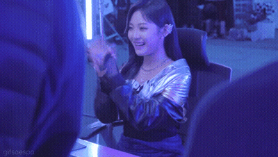 A Woman In A Metallic Jacket Is Sitting In A Chair In A Dark Room . GIF