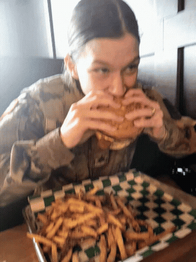 A Woman In A Military Uniform Is Eating A Sandwich And French Fries GIF