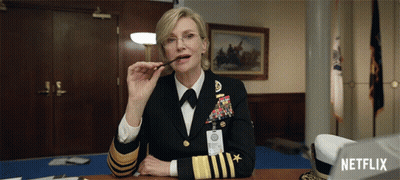 A Woman In A Military Uniform Is Sitting At A Desk With A Netflix Logo In The Background GIF