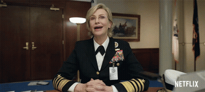 A Woman In A Military Uniform Sits At A Desk With A Netflix Logo In The Corner GIF