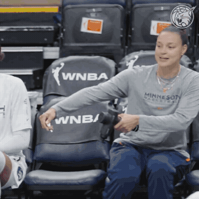 A Woman In A Minnesota Basketball Shirt Sits In A Bleacher GIF