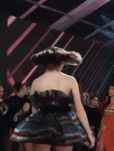 A Woman In A Multicolored Dress Is Dancing In A Crowd . GIF