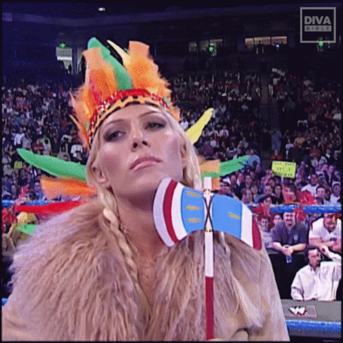 A Woman In A Native American Costume Holds A Flag In Front Of A Diva Studios Sign GIF