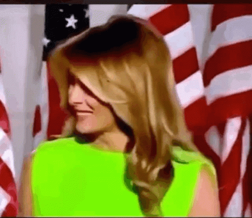 A Woman In A Neon Green Dress Is Standing In Front Of A Flag . GIF