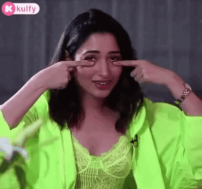 A Woman In A Neon Green Jacket Is Pointing At Her Eye . GIF