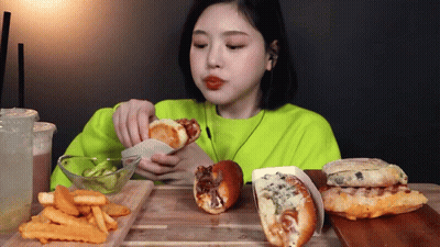 A Woman In A Neon Green Sweater Is Eating French Fries And Hamburgers GIF