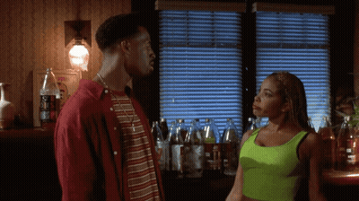 A Woman In A Neon Green Tank Top Stands Next To A Man In A Red Jacket GIF