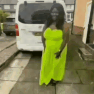 A Woman In A Neon Yellow Dress Is Standing In Front Of A White Van On A Sidewalk . GIF