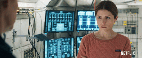 A Woman In A Netflix Sweater Stands In Front Of A Bunch Of Monitors GIF