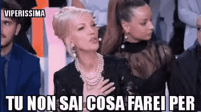 A Woman In A Pearl Necklace Is Sitting In Front Of A Group Of People With Her Hand On Her Chest . GIF
