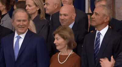 A Woman In A Pearl Necklace Stands Between Two Men In Suits And Ties GIF