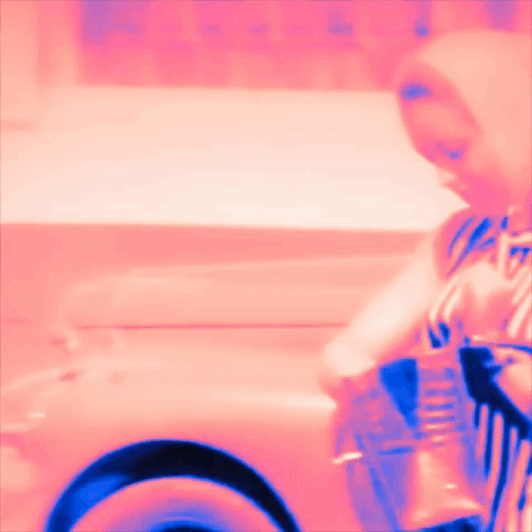 A Woman In A Pink And Blue Striped Dress Is Holding A Cup GIF