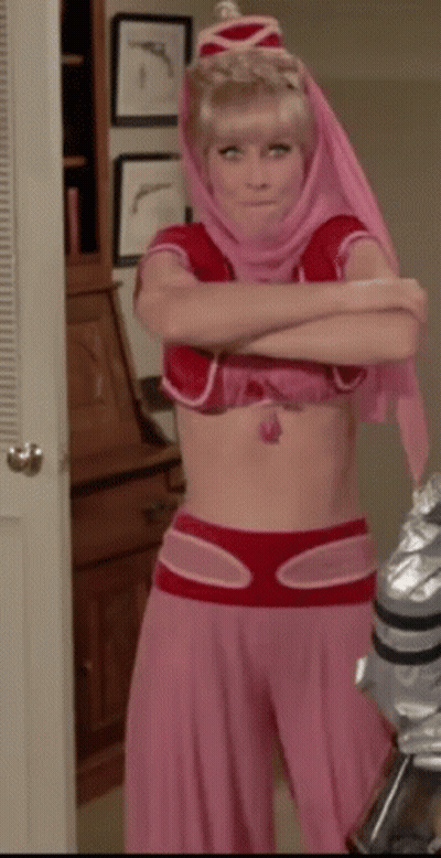 A Woman In A Pink And Red Costume With Her Arms Crossed Is Standing In A Room . GIF