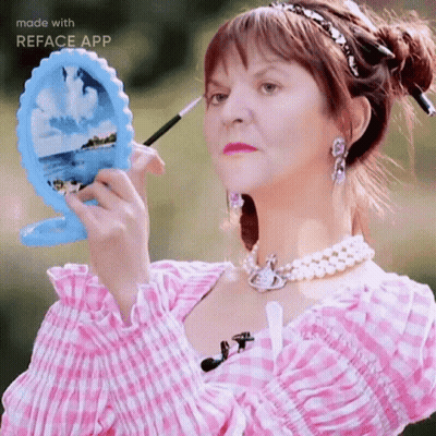 A Woman In A Pink And White Plaid Dress Is Applying Makeup GIF