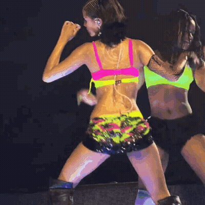A Woman In A Pink Bra And Neon Shorts Is Dancing On A Stage GIF