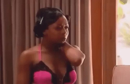 A Woman In A Pink Bra Is Standing In Front Of A Window And Holding Her Neck . GIF