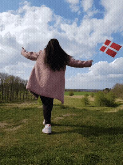 A Woman In A Pink Coat Holds A Red And White Flag In A Field GIF