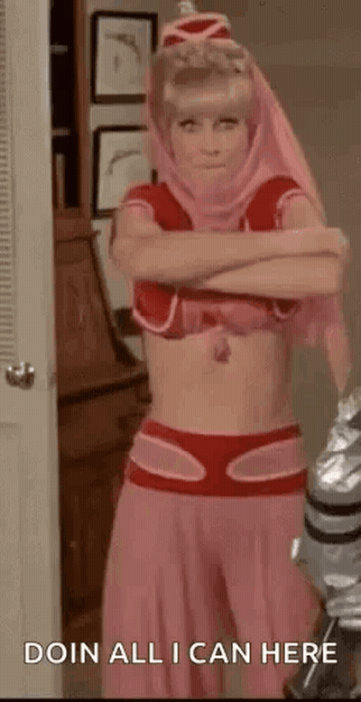 A Woman In A Pink Costume Is Standing In A Room With Her Arms Crossed And A Robot In The Background . GIF