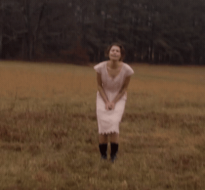 A Woman In A Pink Dress And Black Boots Stands In A Field GIF