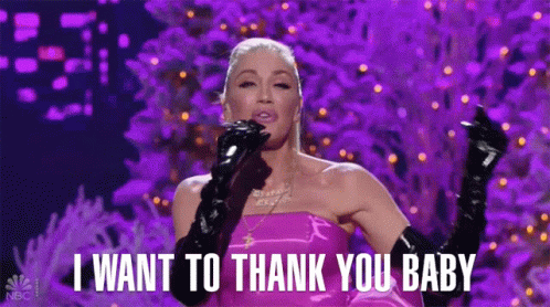 A Woman In A Pink Dress And Black Gloves Is Standing On A Stage And Singing . GIF