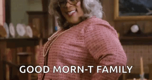 A Woman In A Pink Dress And Glasses Is Saying `` Good Morning - T Family '' . GIF