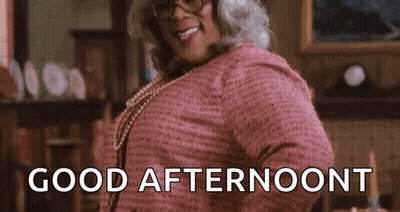 A Woman In A Pink Dress And Glasses Is Standing In A Room And Smiling . GIF