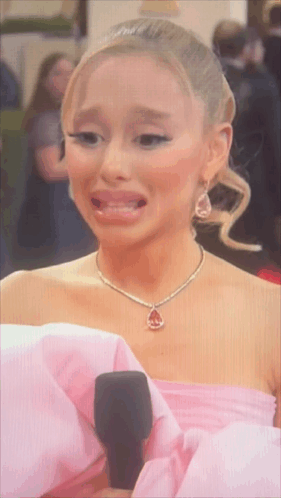 A Woman In A Pink Dress And Necklace Is Crying GIF