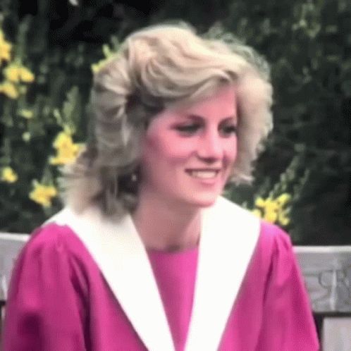 A Woman In A Pink Dress And White Collar Is Smiling . GIF