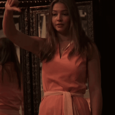 A Woman In A Pink Dress Has The Letter S On Her Necklace GIF