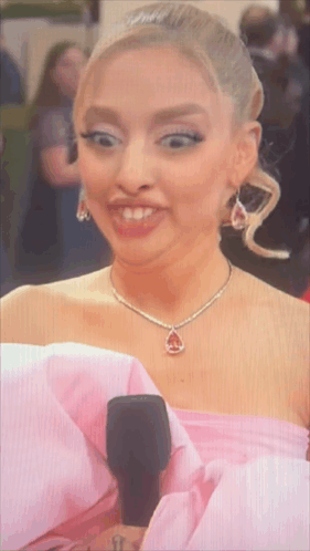 A Woman In A Pink Dress Holds A Microphone And Makes A Funny Face GIF